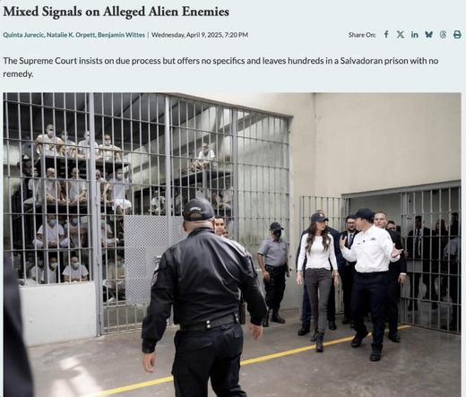 The image depicts a scene inside a prison in El Salvador, featuring several individuals in white clothing and face masks seated in a cell. Security personnel, including uniformed officers, are present, with some engaged in conversation. The atmosphere conveys tension and highlights issues