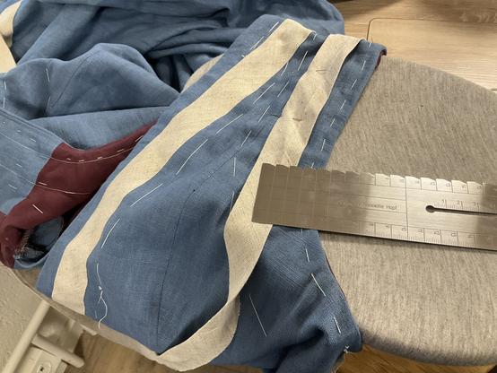 Streifen wird an den Armloch gesteckt. Der Steifen am Halsauschnitt ist schon angenäht. Das Oberteil des Kleides liegt auf einem Bügelbock. lineal zum Abmessen liegt am Armloch.