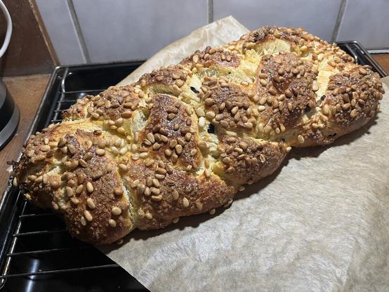 frisch gebackener Osterzopf mit Pinienkernen auf Backpapier auf einem Gitterrost mit Blech