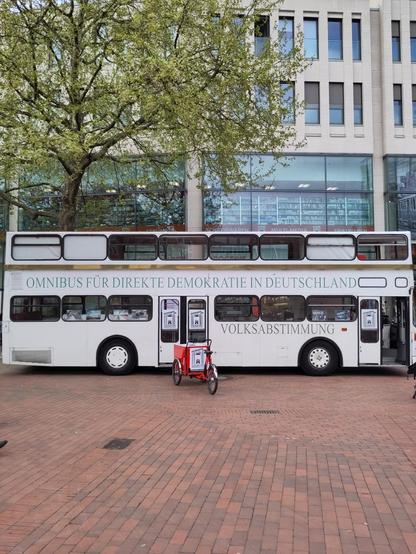 In einer Fußgängerzone: ein weißer Doppeldecker-Bus mit der Aufschrift "Omnibus für direkte Demokratie in Deutschland - Volksabstimmung". Davor eines der Lastenfahrräder. Im Fenster Hamburg Werbefrei-Plakate.