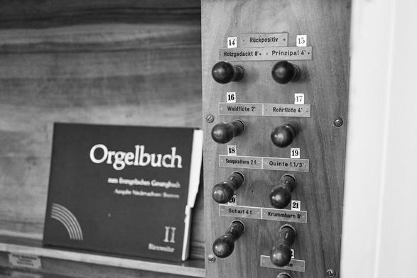 Teilansicht des Bedienpultes einer Kirchenorgel. Zu sehen sind einige Knöpfe der Register und (etwas unscharf) ein Orgelbuch.