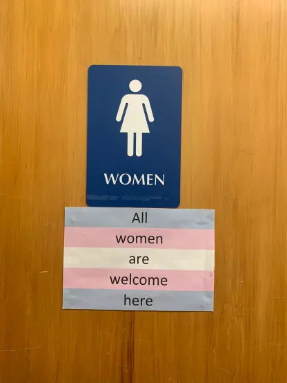 Women's bathroom sign, and trans flag with "All women are welcome here" written