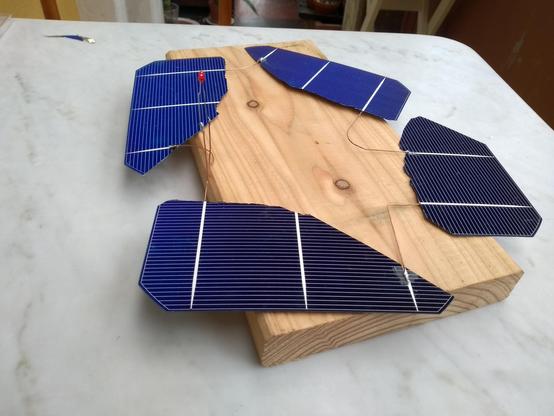 Vier zerbrochene Solarzellen zusammengelötet mit Kupferdrähten, den Kreis schließt eine eingelötete, leuchtende, rote LED.