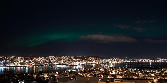 A panoramic view of Tromsø with the aurora borealis in the night sky above the city.