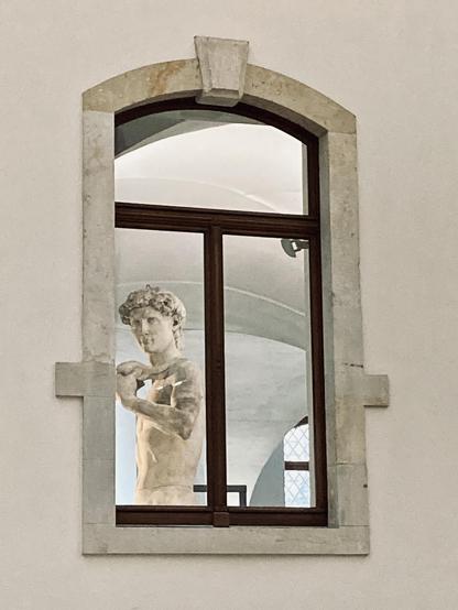 Ein Fenster an einer hellen Fassade, aus der eine Davidstatue schaut.
