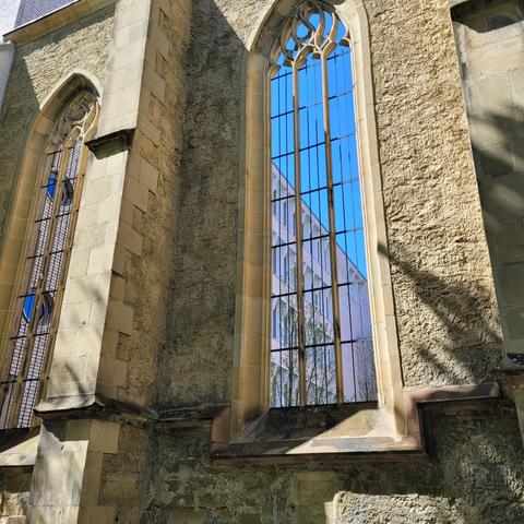 Ein Fenster von aussen. Darin spiegelt sich blauer Himmel und ein anderes Gebäude mit vielen Fenstern