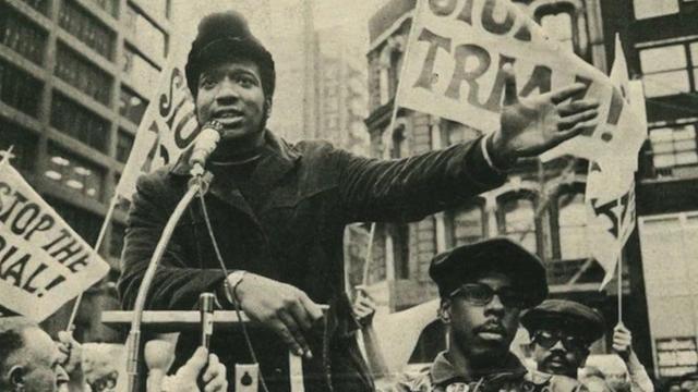 Monochrome photo of Fred Hampton speaking at a microphone during a protest.
