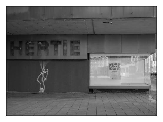 Schaufenster und verrammelter Eingang eines leer stehenden Kaufhauses. Aufschrift "Hertie". Graffiti.