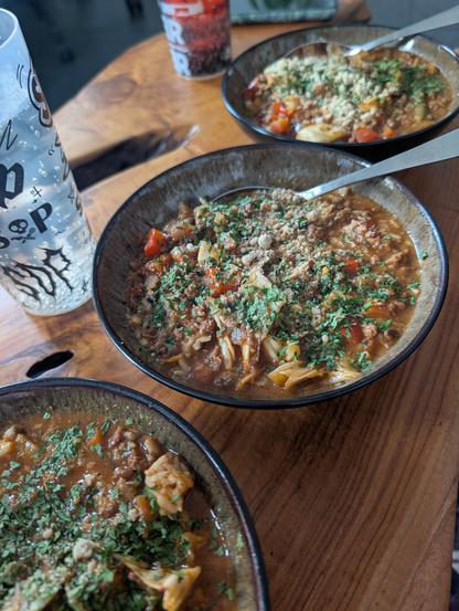 Drei Teller mit einem rot-braunen Eintopf, on top Petersilie und Parmesan