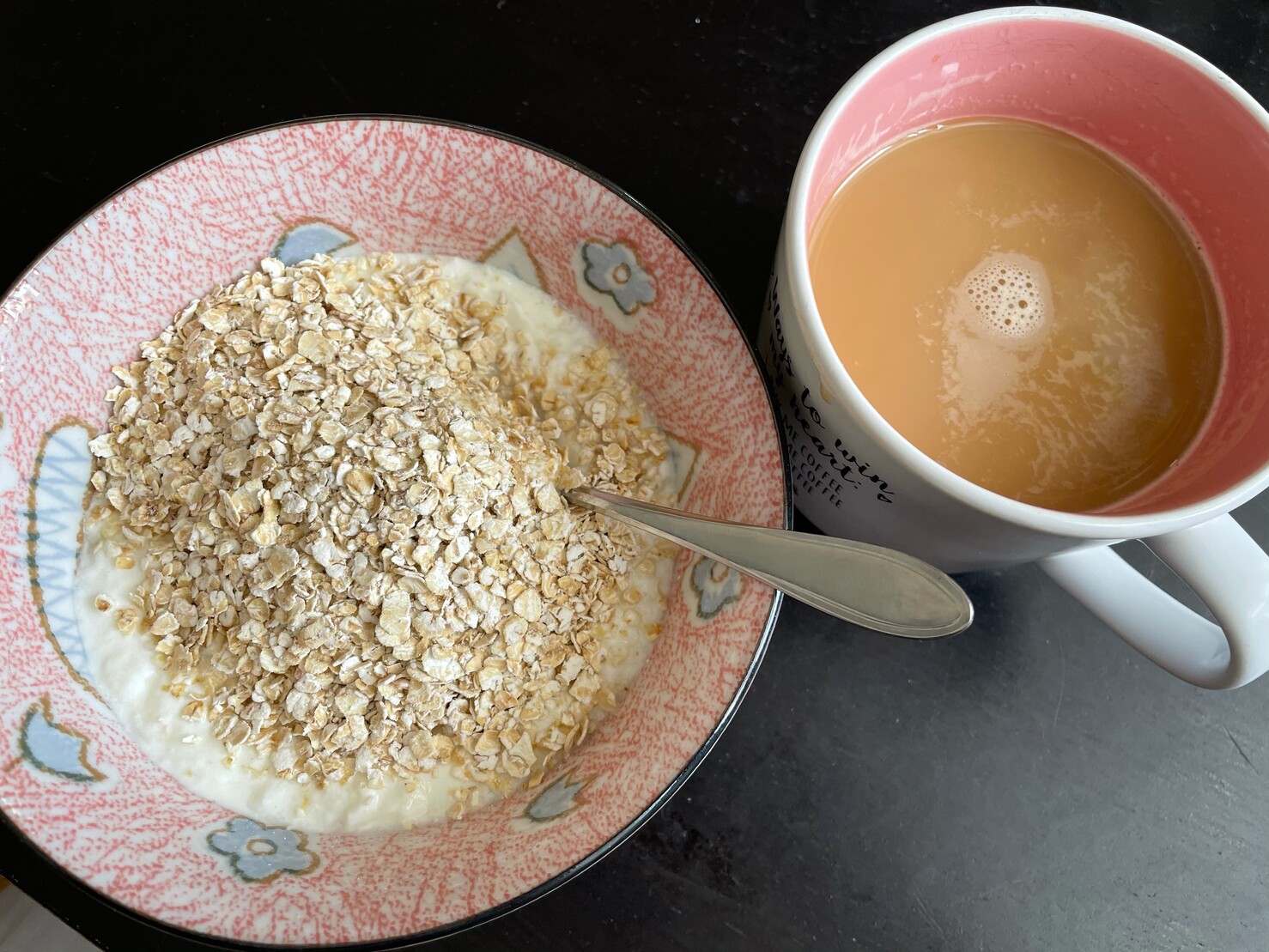 Foto von der Katzenschüssel „in Aktion“ mit Joghurt und Haferflocken, daneben die gefüllte Kaffeetasse