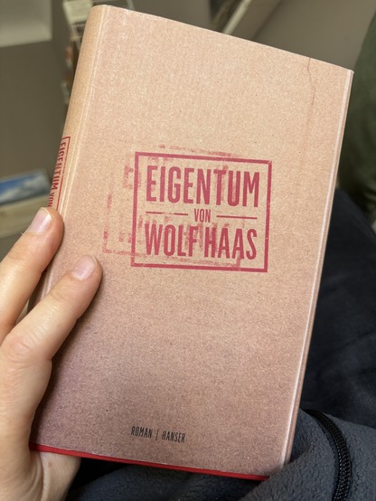 Hand hält ein Buch, bei welchem es sich um Eigentum von Wolf Haas handelt