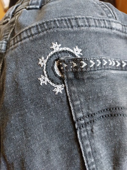 Konzentrische Kreise um die linke obere Ecke der Gesäßtasche einer Jeans. Der äußerste Kreis ist mit kleinen, sternförmigen Noppen besetzt. 
Stichart: Kettstich