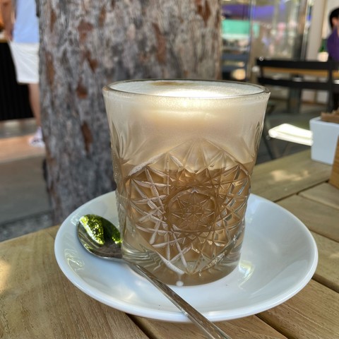 Foto eines gemusterten Glases mit Caffe Latte auf einem Holztisch vor einem Kastanienbaum-Stamm