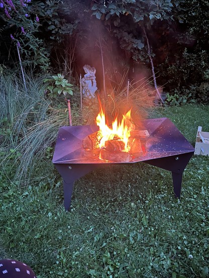 Feuer in einer Feuerschale, im Hintergrund Pflanzen und eine Putte.