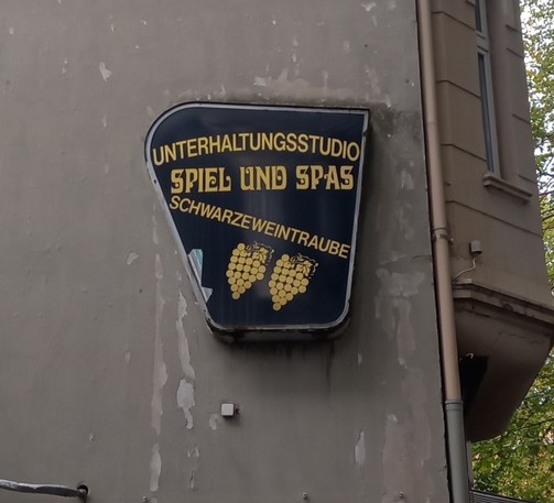 ein schild an einer fassade, das die unterhaltsamkeit einer spielhalle bewirbt; drauf steht: unterhaltungsstudio/spiel & spas/schwarzeweintraube.