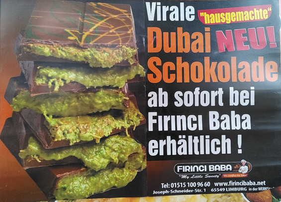 Werbeaufsteller: NEU!
Virale „hausgemachte“ Dubai Schokolade
ab sofort bei Fırıncı Baba erhältlich!
(Adresse)
Dazu ein Foto eines Stapels von gefüllten Schokoladentafeln. Die Füllung ist grün-braun und lauft aus den Tafeln heraus, erinnert an 🤮